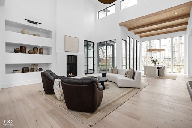 living room featuring built in shelves, beamed ceiling, a towering ceiling, wood ceiling, and light wood-type flooring