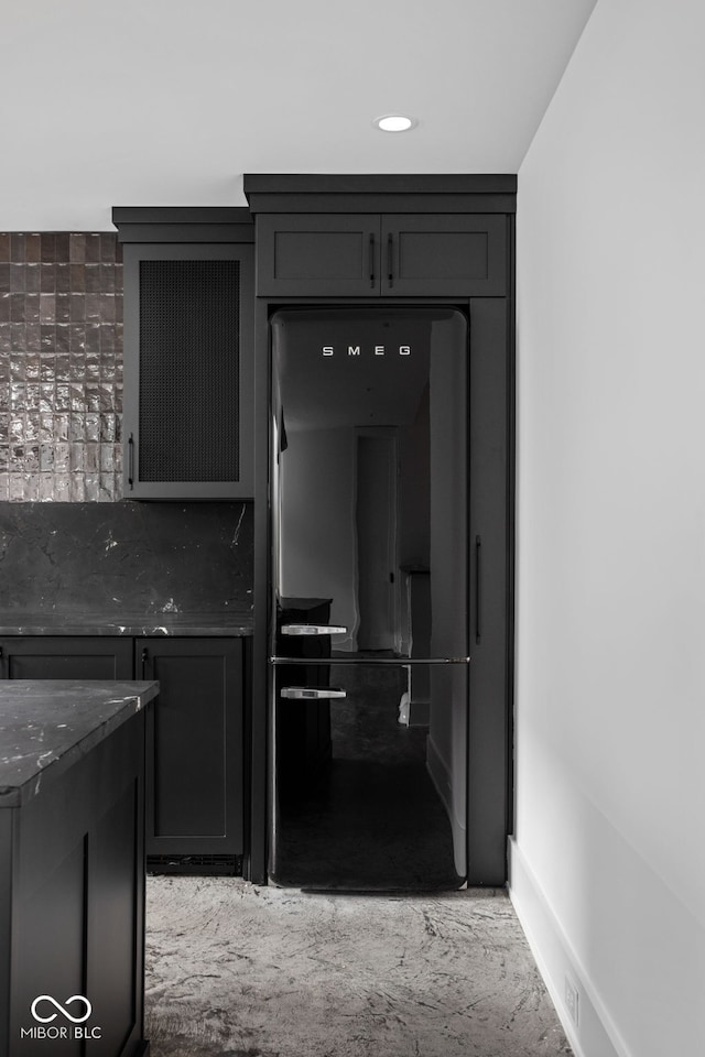 kitchen featuring decorative backsplash, refrigerator, and dark stone countertops