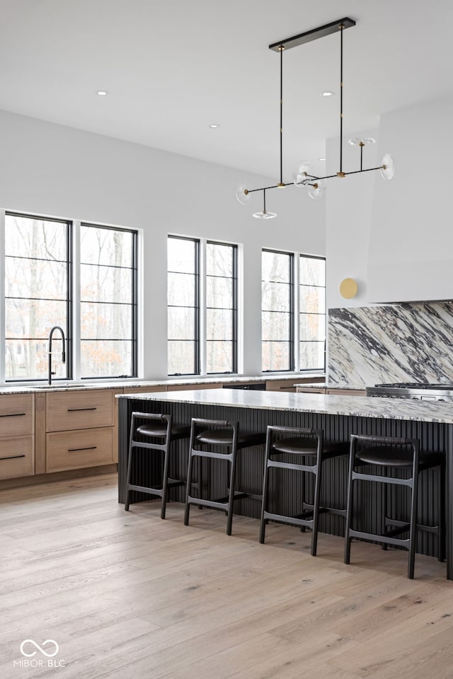 kitchen featuring decorative backsplash, light hardwood / wood-style floors, a kitchen bar, and hanging light fixtures