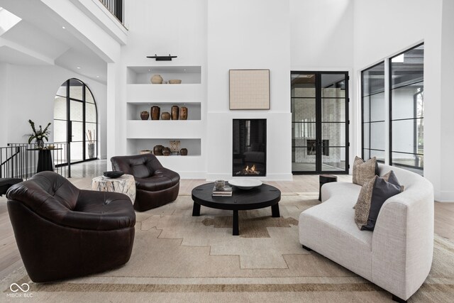 living room with a high ceiling, light hardwood / wood-style floors, built in features, and french doors