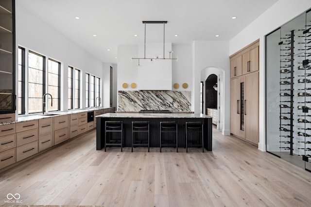 kitchen featuring pendant lighting, backsplash, a spacious island, light hardwood / wood-style flooring, and a kitchen bar