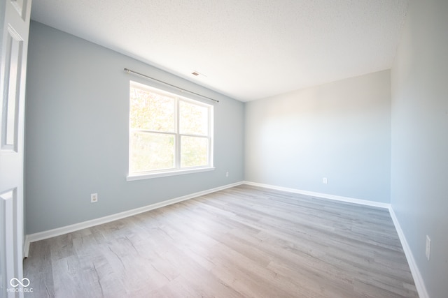 empty room with a textured ceiling and light hardwood / wood-style flooring