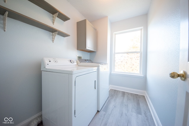 laundry room featuring cabinets, washing machine and clothes dryer, and light hardwood / wood-style flooring