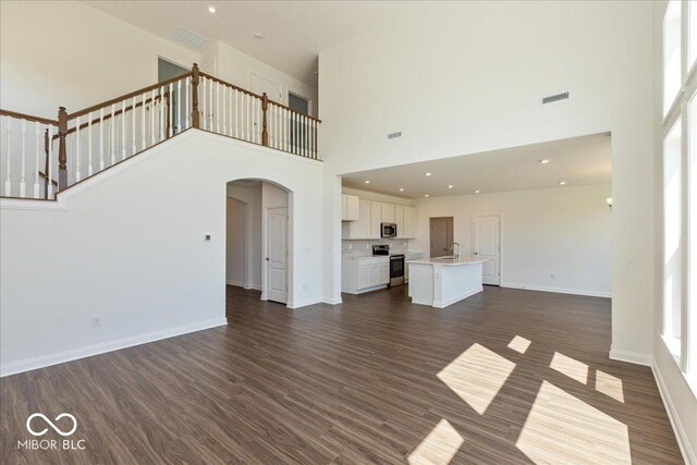 1105 Gatewick Ct, Greenwood, IN 46143 - unfurnished living room featuring a towering ceiling, a sink, arched walkways, dark wood-style flooring, and baseboards