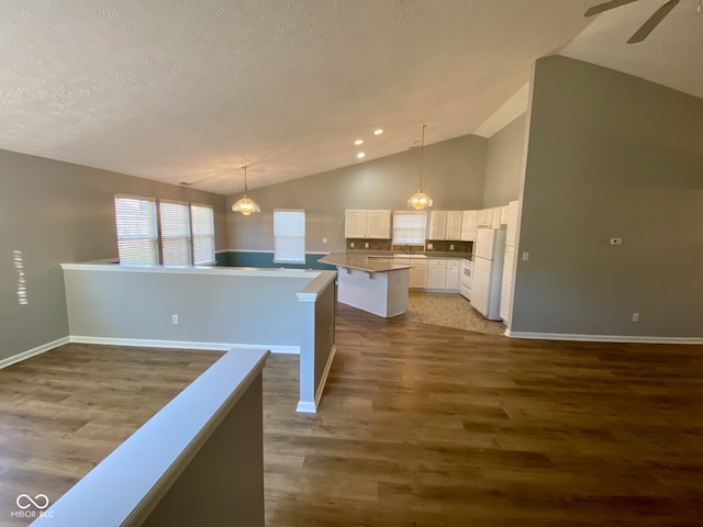 kitchen with white cabinetry, white refrigerator, hanging light fixtures, vaulted ceiling, and dark wood-type flooring