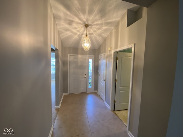 entrance foyer featuring a chandelier, a textured ceiling, light tile patterned floors, and vaulted ceiling