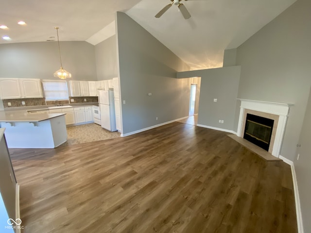 unfurnished living room featuring sink, ceiling fan with notable chandelier, plenty of natural light, high vaulted ceiling, and light wood-type flooring