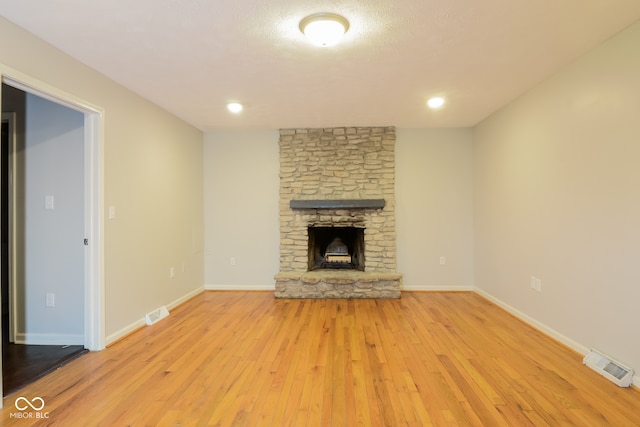 unfurnished living room featuring a stone fireplace and light hardwood / wood-style flooring