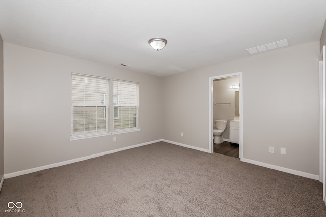 unfurnished bedroom featuring ensuite bathroom and dark colored carpet