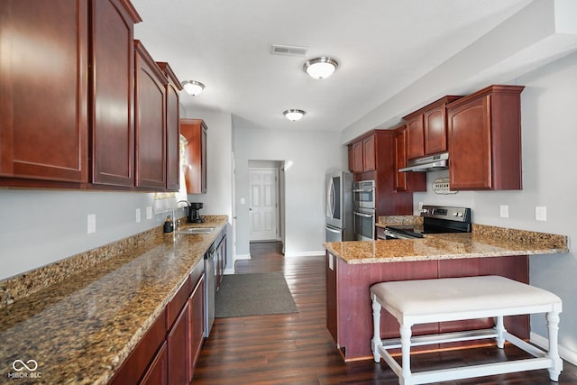 kitchen with stainless steel appliances, sink, light stone counters, a breakfast bar area, and dark wood-type flooring