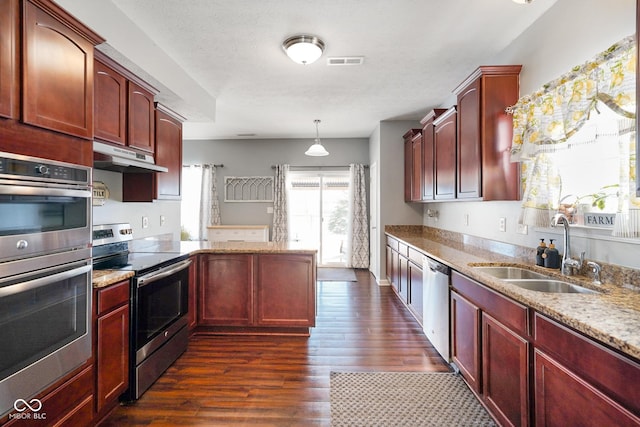 kitchen featuring stainless steel appliances, hanging light fixtures, light stone countertops, dark wood-type flooring, and sink