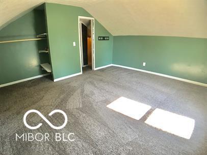 additional living space featuring dark colored carpet and lofted ceiling