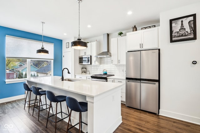 kitchen featuring wall chimney exhaust hood, stainless steel appliances, sink, a center island with sink, and white cabinetry