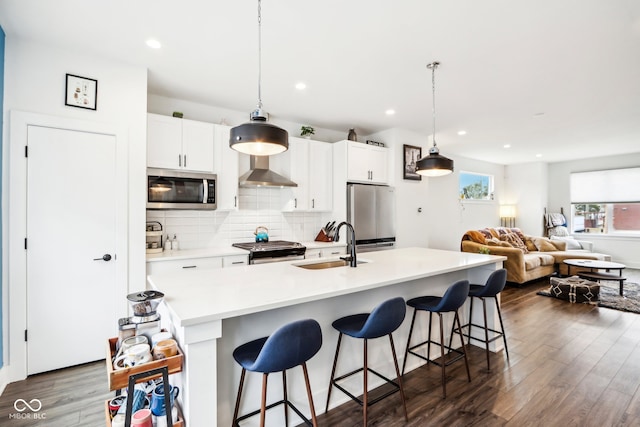 kitchen with dark hardwood / wood-style flooring, stainless steel appliances, hanging light fixtures, and an island with sink