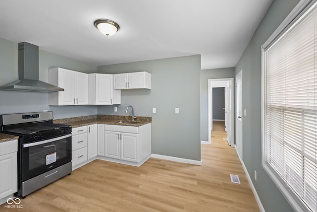 kitchen with white cabinets, wall chimney exhaust hood, sink, stainless steel gas range oven, and light wood-type flooring