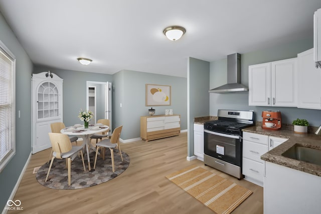 kitchen with dark stone counters, wall chimney exhaust hood, stainless steel range, white cabinetry, and light hardwood / wood-style flooring