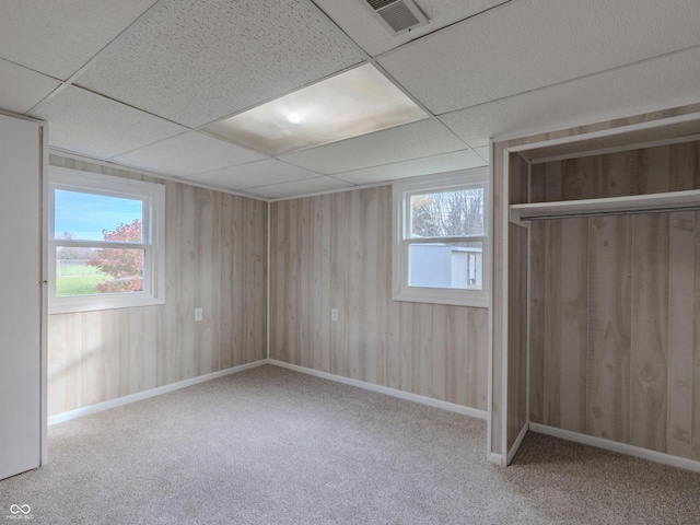 unfurnished bedroom featuring wood walls, a paneled ceiling, carpet floors, and a closet