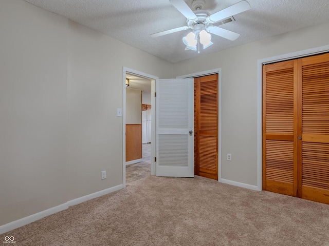 unfurnished bedroom featuring a textured ceiling, multiple closets, light carpet, and ceiling fan