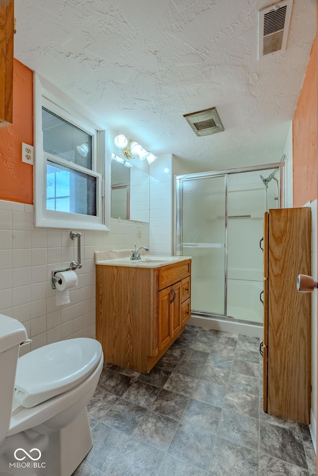 bathroom with tile walls, walk in shower, a textured ceiling, and vanity