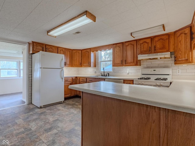 kitchen with white appliances, sink, backsplash, and kitchen peninsula