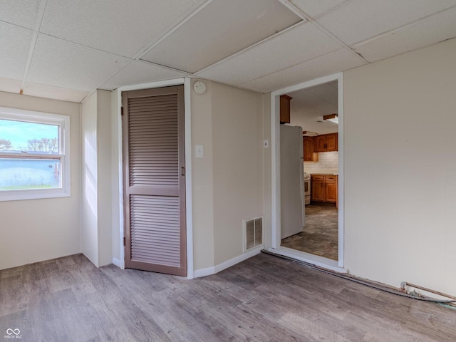 spare room with a drop ceiling and light hardwood / wood-style floors