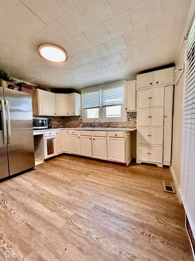 kitchen with decorative backsplash, appliances with stainless steel finishes, sink, and light hardwood / wood-style flooring