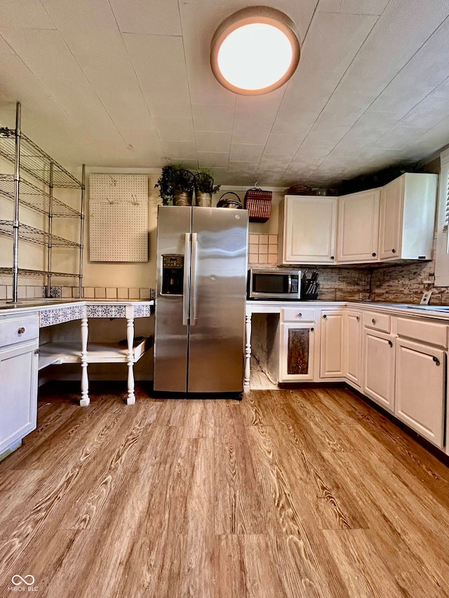 kitchen with stainless steel appliances, white cabinets, light hardwood / wood-style flooring, and backsplash