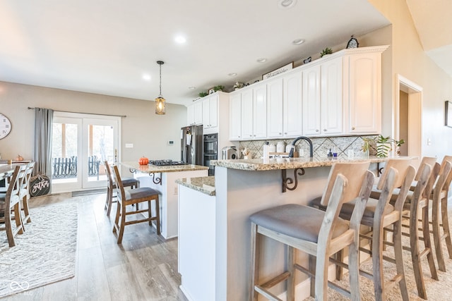 kitchen featuring a kitchen breakfast bar, light stone counters, decorative light fixtures, light hardwood / wood-style floors, and white cabinetry