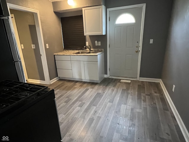 kitchen with stainless steel fridge, light wood-type flooring, black stove, sink, and white cabinets