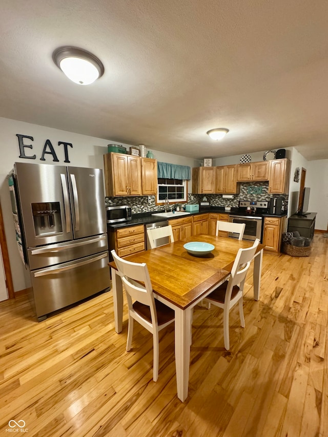 kitchen with stainless steel appliances, a textured ceiling, sink, decorative backsplash, and light hardwood / wood-style floors