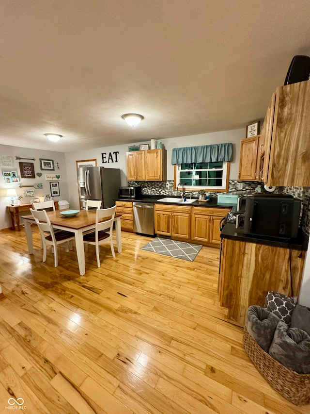 kitchen with sink, light wood-type flooring, appliances with stainless steel finishes, and decorative backsplash