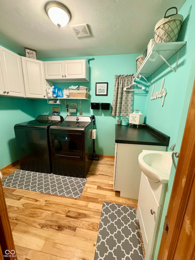 laundry area with a textured ceiling, cabinets, sink, washer and dryer, and light hardwood / wood-style flooring