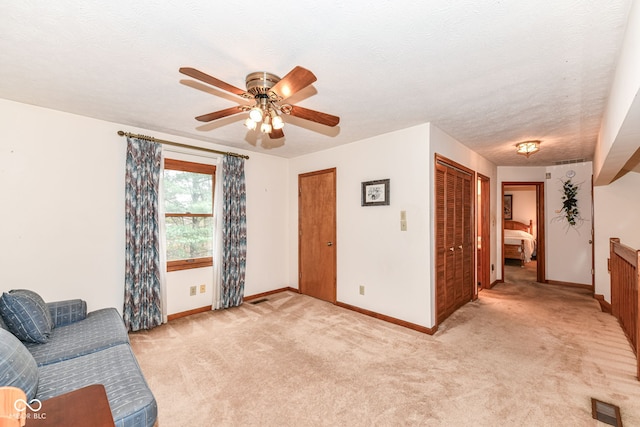 living area with ceiling fan, light colored carpet, and a textured ceiling