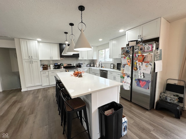 kitchen with wood-type flooring, white cabinetry, pendant lighting, and appliances with stainless steel finishes