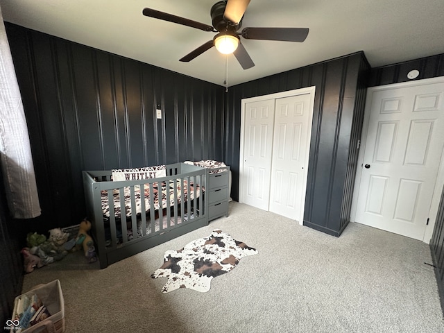 carpeted bedroom with a nursery area, ceiling fan, and a closet