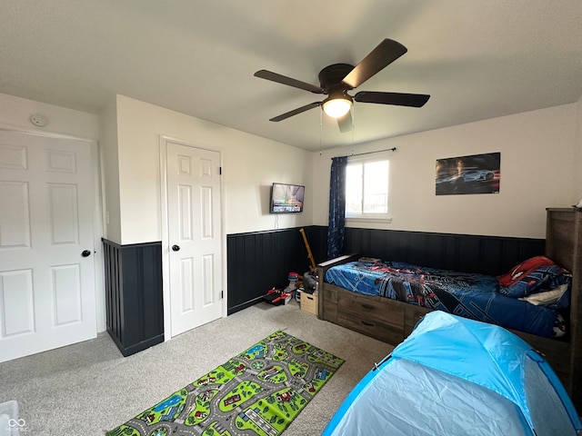 carpeted bedroom featuring wood walls and ceiling fan