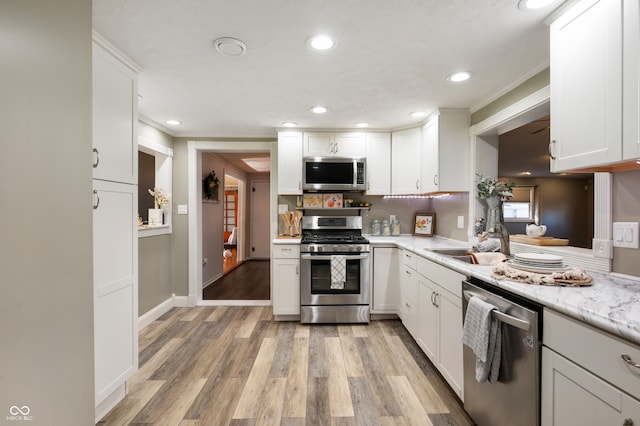 kitchen with light stone counters, light hardwood / wood-style flooring, sink, white cabinetry, and appliances with stainless steel finishes