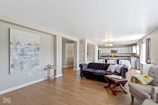 living room with a textured ceiling, an inviting chandelier, and light hardwood / wood-style flooring