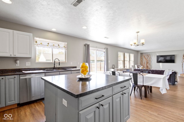 kitchen featuring light wood-type flooring, stainless steel dishwasher, gray cabinetry, a textured ceiling, and a center island