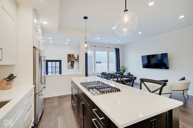 kitchen with stainless steel refrigerator, hanging light fixtures, white cabinets, a kitchen island, and dark wood-type flooring