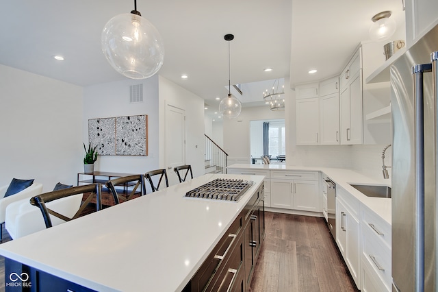 kitchen featuring stainless steel appliances, white cabinetry, decorative light fixtures, a kitchen island, and dark hardwood / wood-style flooring