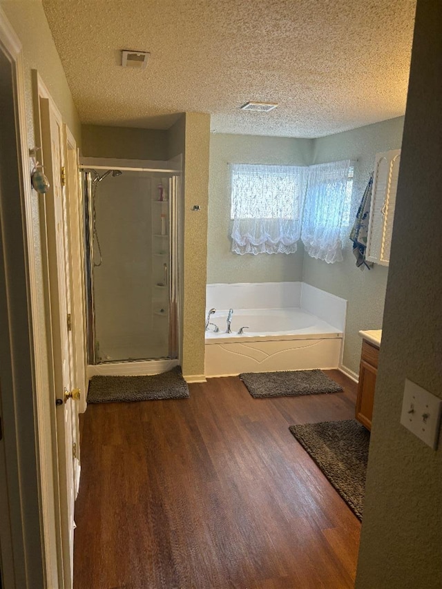 bathroom with a textured ceiling, wood finished floors, a bath, and a shower stall