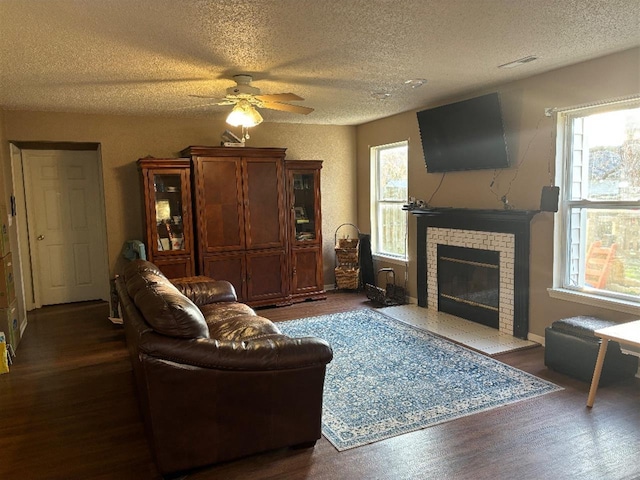 living room featuring dark wood-style floors, visible vents, a fireplace, and a wealth of natural light