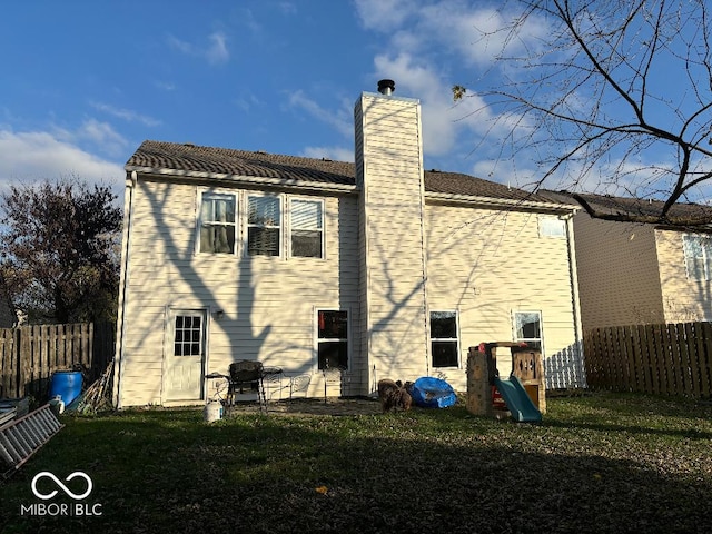 back of house featuring a playground, a lawn, a chimney, and fence