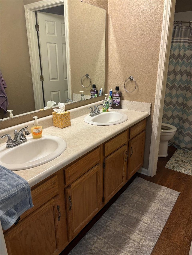 bathroom with wood finished floors, a sink, toilet, and double vanity