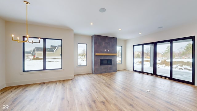 unfurnished living room featuring a tiled fireplace, light hardwood / wood-style floors, and an inviting chandelier