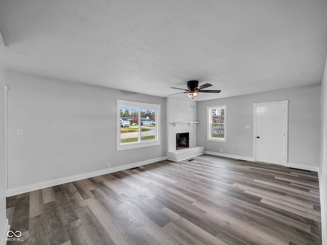 unfurnished living room with hardwood / wood-style flooring, ceiling fan, a fireplace, and a wealth of natural light