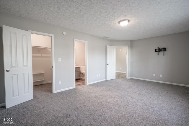 unfurnished bedroom featuring a textured ceiling, carpet floors, a spacious closet, connected bathroom, and a closet