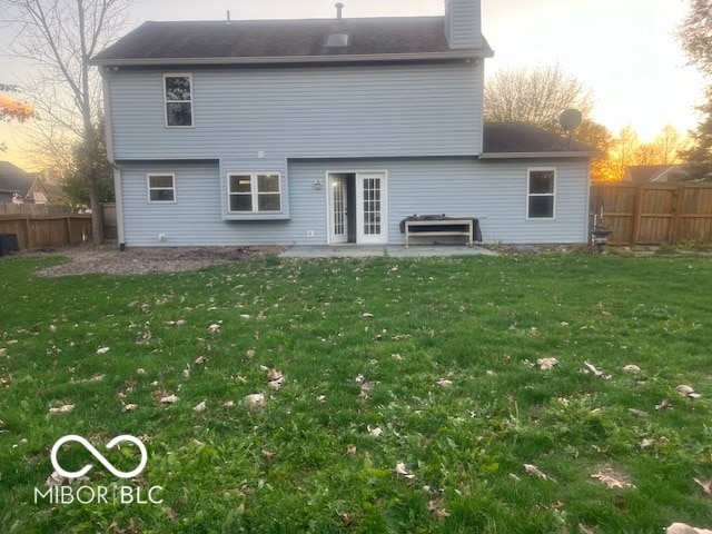 back house at dusk featuring a lawn and french doors