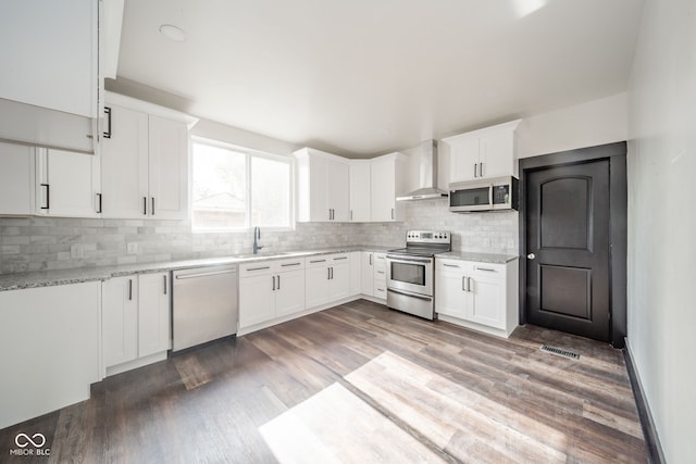 kitchen with white cabinetry, appliances with stainless steel finishes, backsplash, dark wood-type flooring, and wall chimney range hood